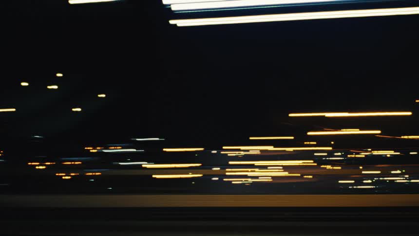An abstract long-exposure view from a moving vehicle captures streaks of colorful lights while driving through a city and tunnel at night