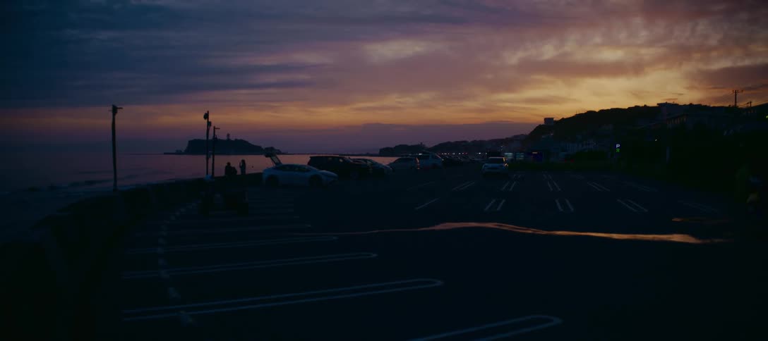 A quiet coastal parking lot overlooks the ocean and a distant island under a beautiful sunset sky in Japan