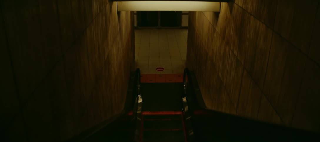 A moody point-of-view shot descends a dark, empty escalator into an underground subway station