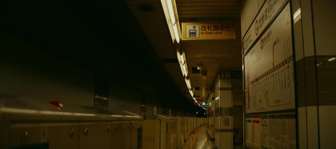A silent, empty hallway lined with lockers inside a dimly lit Japanese underground subway station
