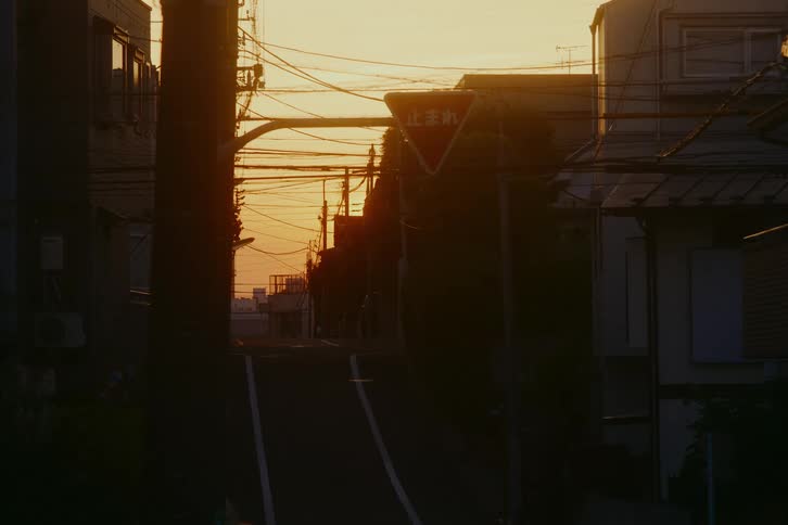 A quiet residential street in Japan is silhouetted by the warm glow of the setting sun