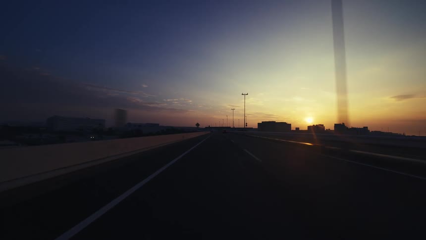 A POV shot captures a serene drive on a highway into the golden sunrise as a large truck overtakes