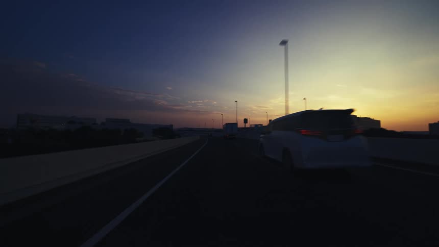 A point-of-view shot from a car driving down an urban highway directly into the beautiful, glowing sunrise