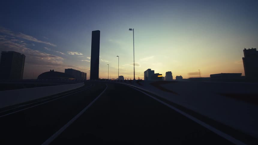 A serene point-of-view drive on a modern highway towards a city skyline silhouetted by the beautiful morning sunrise