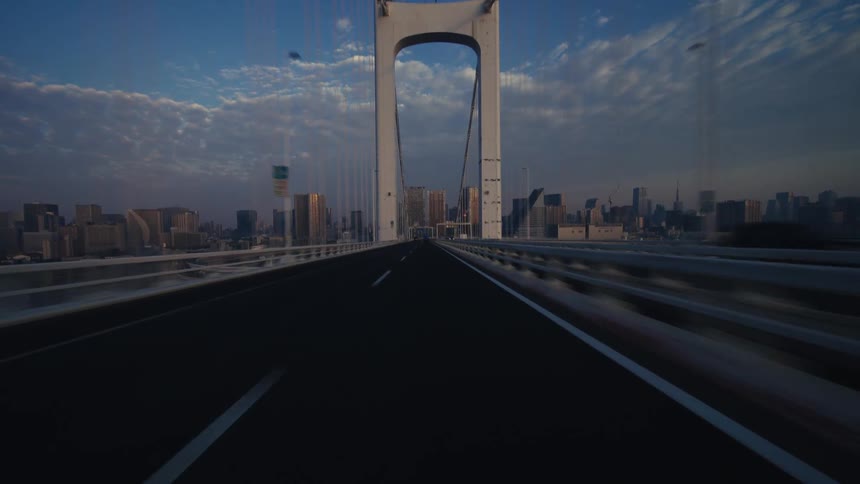 A fast-paced point-of-view driving across the iconic Rainbow Bridge in Tokyo, Japan, towards the city skyline at sunrise