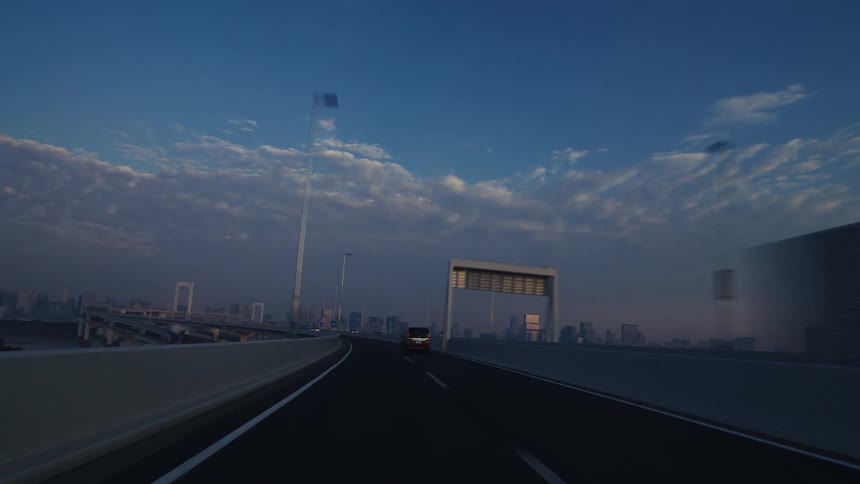 POV driving on the Rainbow Bridge highway overlooking the Tokyo cityscape at dawn under a beautiful cloudy sky