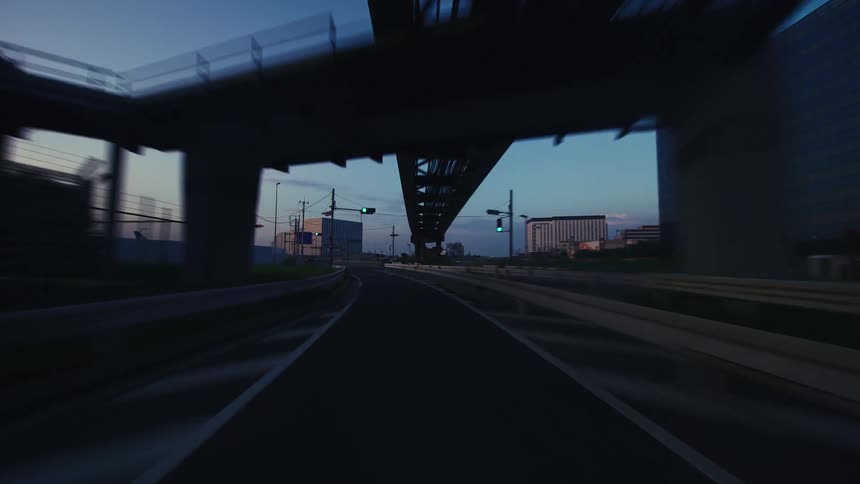 POV driving on an empty urban road under an elevated monorail track at dusk