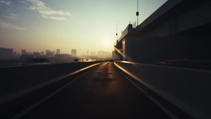 A cinematic point-of-view timelapse driving on a modern highway into a hazy city at sunrise