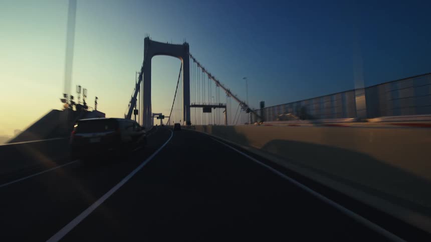 A cinematic point-of-view drive across a modern suspension bridge into the city at sunrise