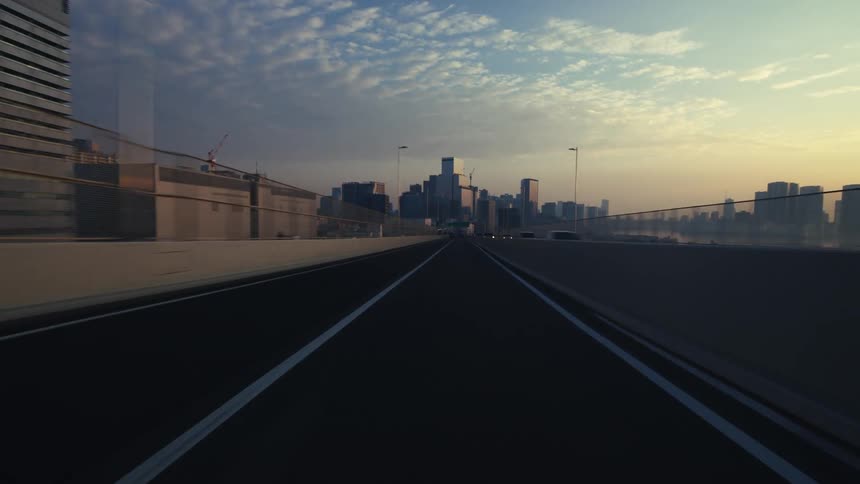 A first-person point of view driving on an urban highway towards a city skyline during a beautiful sunrise