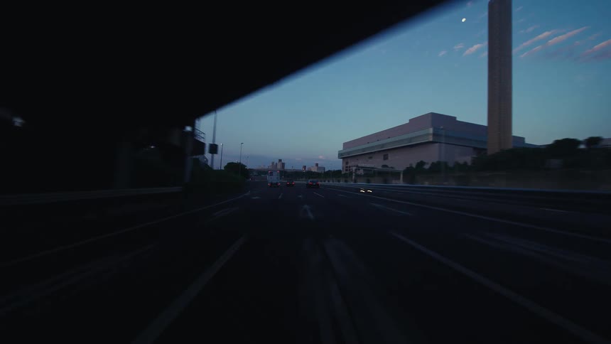 A cinematic point-of-view shot of a car driving down a highway at dusk, passing under several overpasses