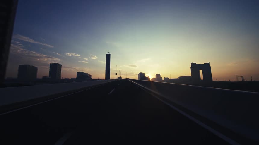 A serene POV drive along an empty city overpass towards the glowing horizon at dawn