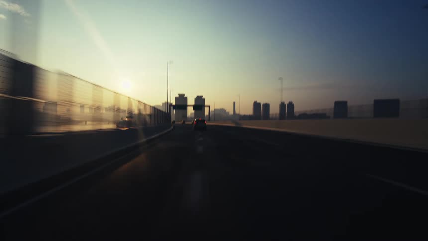 A point-of-view shot driving along a city highway bridge towards the skyline during a beautiful golden sunrise
