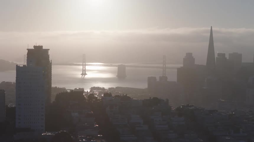A hazy sunrise over the San Francisco skyline with the Bay Bridge and Transamerica Pyramid visible through the fog