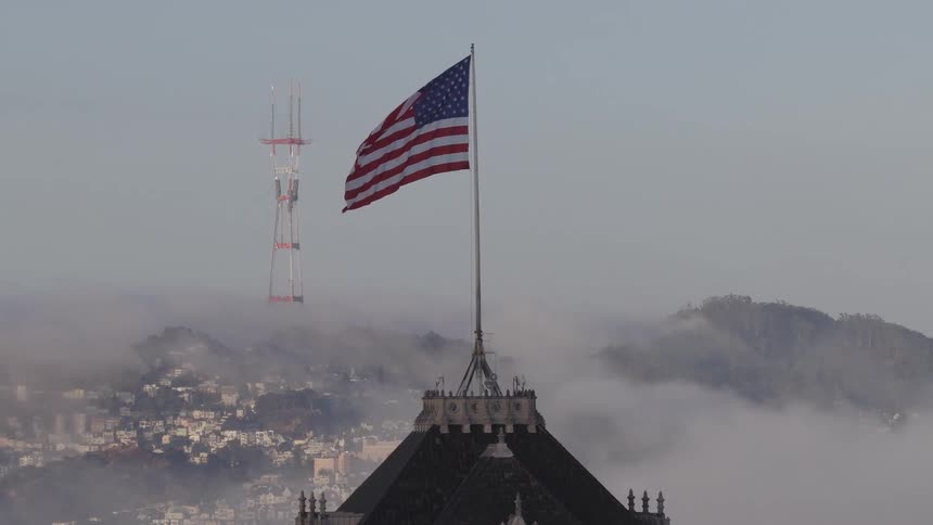 Slow pan reveals an American flag waving atop a building with San Francisco's Sutro Tower in the foggy background