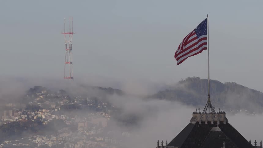 An American flag waves proudly over a foggy San Francisco skyline with the iconic Sutro Tower visible in the background