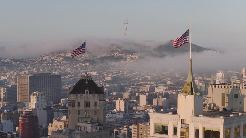 American flags wave over the San Francisco skyline as fog covers the distant hills at sunrise