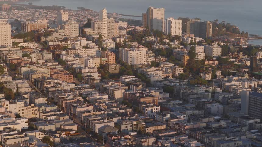 An aerial view of a San Francisco neighborhood slowly tilts up to reveal the bay and the Golden Gate Bridge at sunset