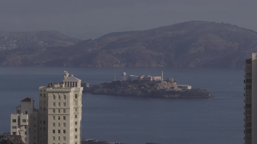A slow zoom out reveals a view of Alcatraz Island in the San Francisco Bay, framed between two high-rise buildings