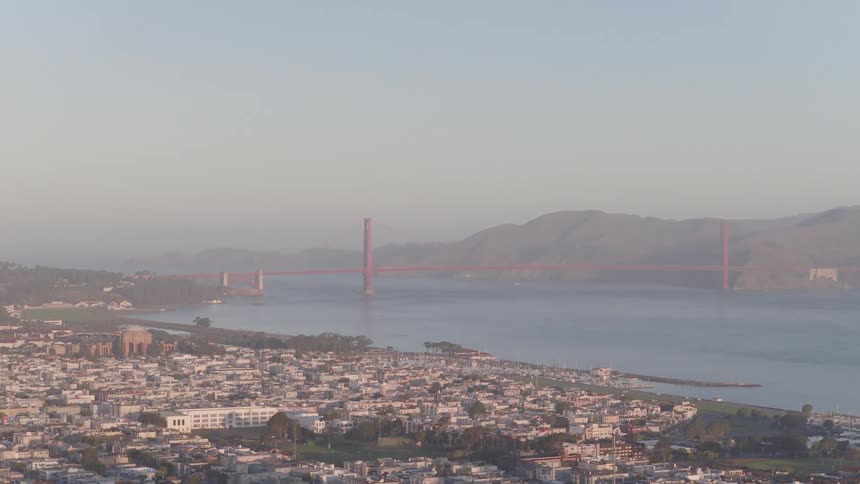 A slow aerial ascent reveals the sprawling city of San Francisco, the bay, and the iconic Golden Gate Bridge in the hazy distance