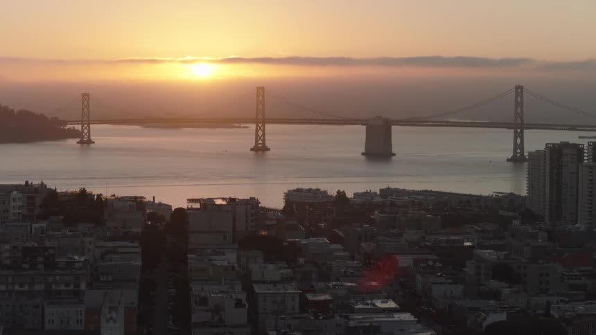 An aerial view pushing towards the San Francisco Bay Bridge over the city during a beautiful hazy sunrise