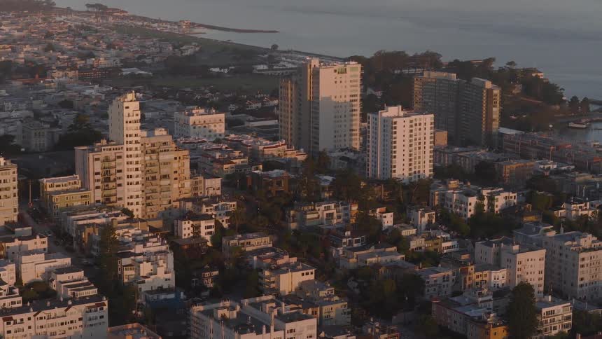 A slow aerial pan reveals a dense coastal city neighborhood with buildings bathed in the warm light of sunrise