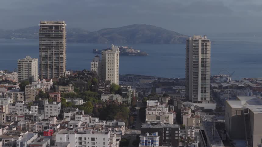 An aerial view pulls back from the dense cityscape of San Francisco, revealing the bay with Alcatraz Island and a passing cargo ship in the distance