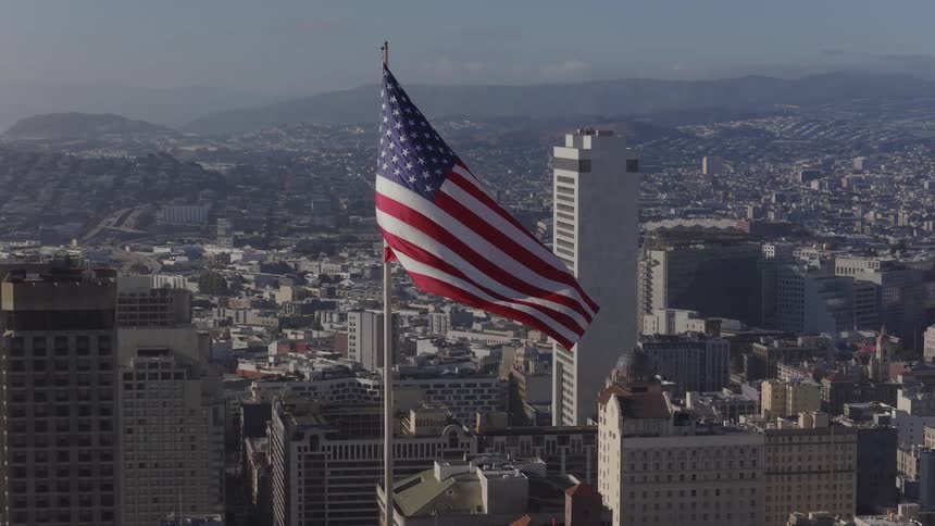 An American flag waves in slow motion, with the expansive cityscape of San Francisco serving as a patriotic backdrop