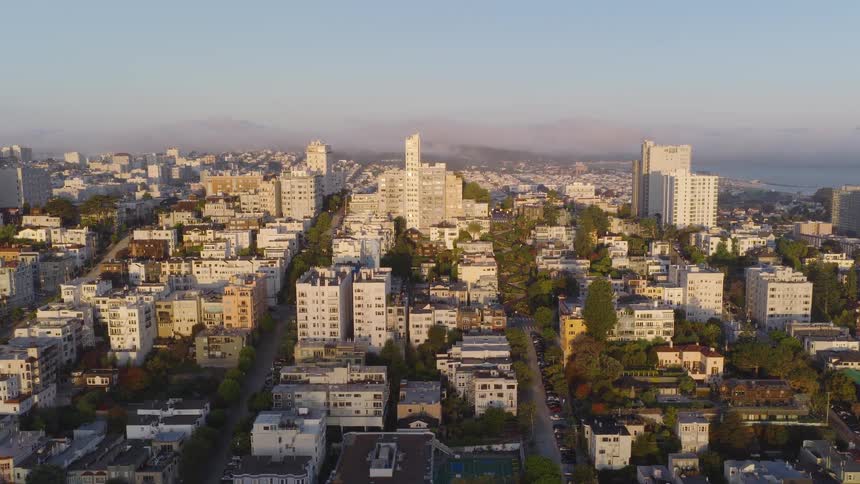 A slow aerial push-in shot reveals the iconic Lombard Street in San Francisco during a beautiful, foggy sunrise