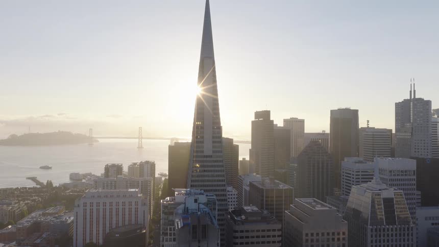 Aerial pull-back shot of the sun rising behind the Transamerica Pyramid, revealing the San Francisco skyline and the bay