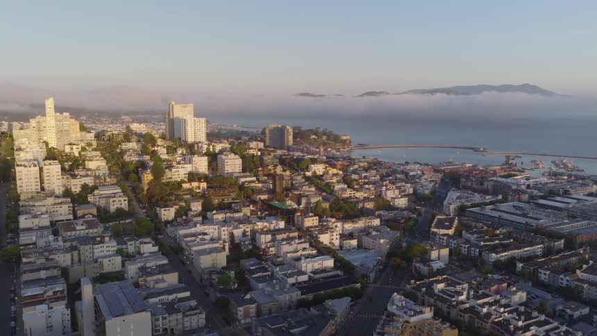 A beautiful aerial view of San Francisco's coastal cityscape bathed in golden sunrise light with fog over the bay