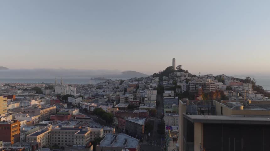 An ascending aerial shot reveals the iconic Coit Tower on Telegraph Hill overlooking the San Francisco Bay at sunrise
