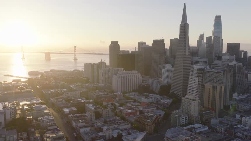 An aerial view captures the San Francisco skyline, including the Transamerica Pyramid and the Bay Bridge, illuminated by the warm glow of a beautiful sunrise