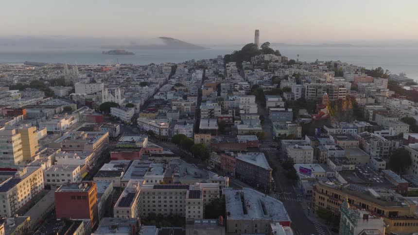 A slow aerial pullback reveals the iconic Coit Tower on Telegraph Hill in San Francisco at sunrise, with Alcatraz Island visible in the bay