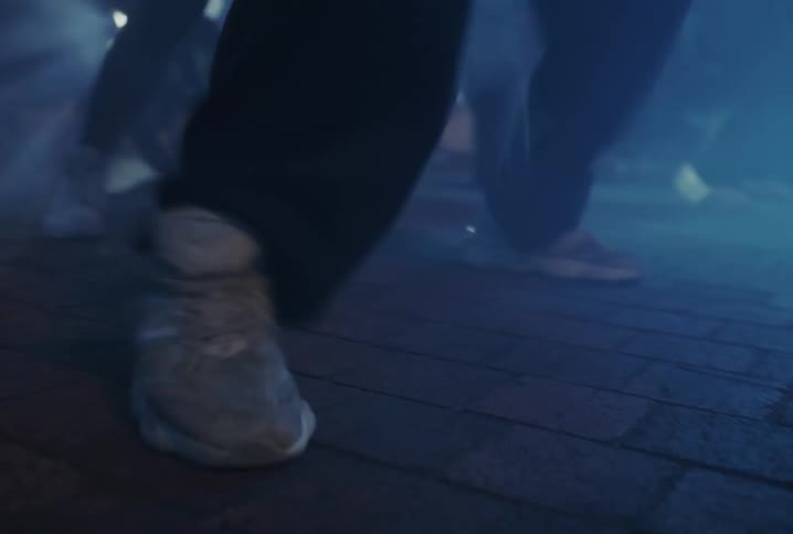 Close-up of people's feet running through a hazy city street at night with blue atmospheric lighting