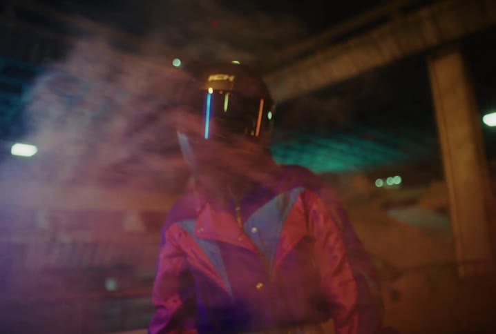 A mysterious biker in a colorful retro jacket and full-face helmet stands in a smoky, neon-lit urban environment at night