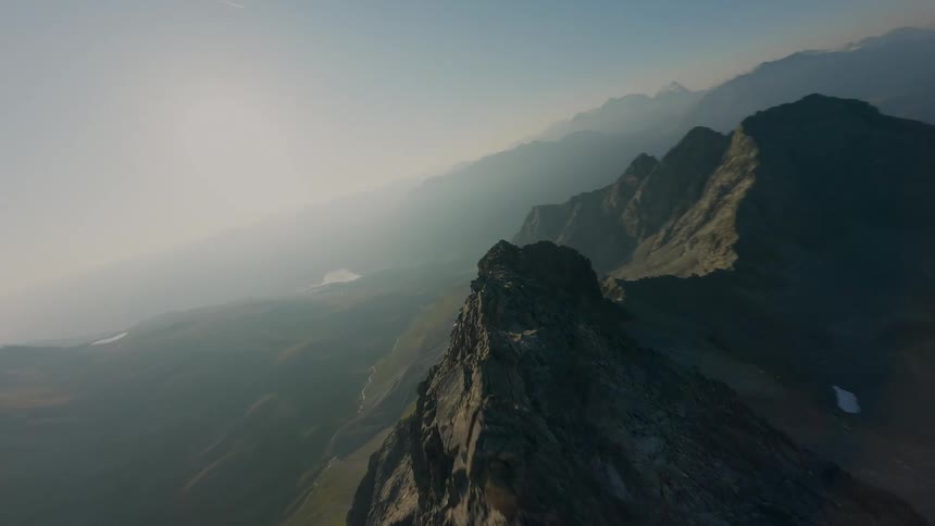 Dynamic FPV drone footage soars along a steep mountain crest, revealing a vast, hazy landscape at sunrise