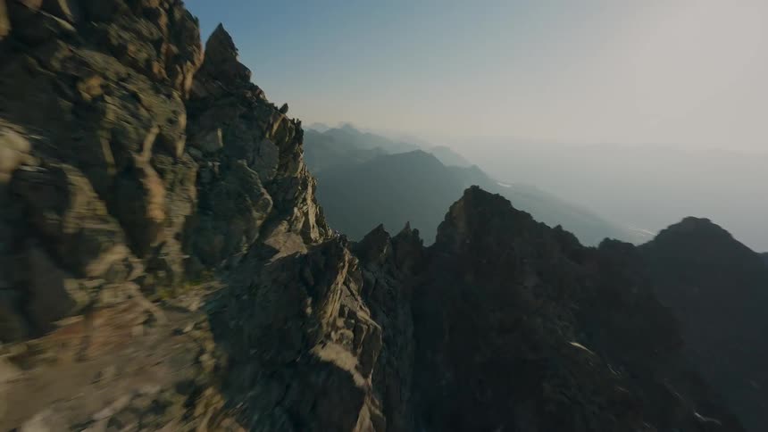 An epic FPV drone shot soars past a climber on a high-altitude mountain ridge, opening up to a spectacular panoramic view of the alpine valley