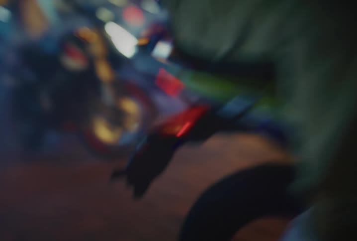 A mysterious motorcyclist emerges from the smoke on a blurry, neon-lit city street at night