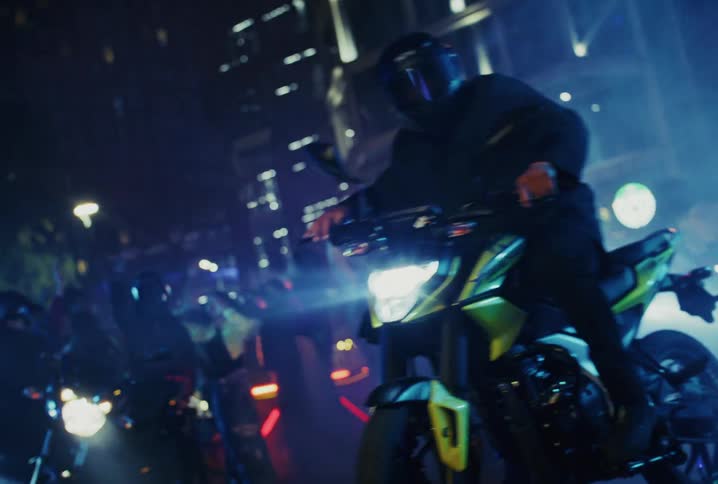 A biker in a helmet performs a stylish wheelie on a modern motorcycle in front of an excited crowd on a city street at night