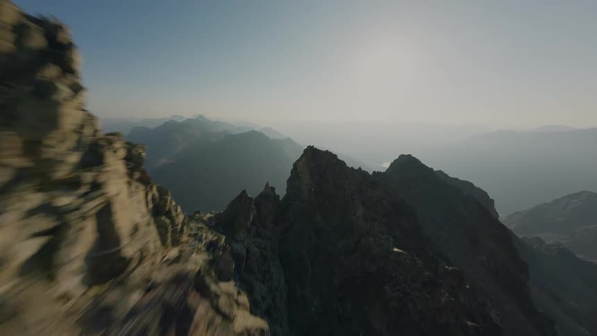 A fast-paced aerial shot follows a lone hiker navigating a sharp, rocky mountain crest before soaring up to reveal the vast, beautiful landscape