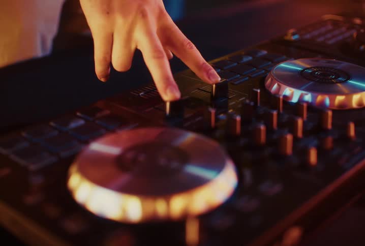 A close-up shot shows a DJ's hand adjusting the faders on a mixing console in a warm, atmospheric light