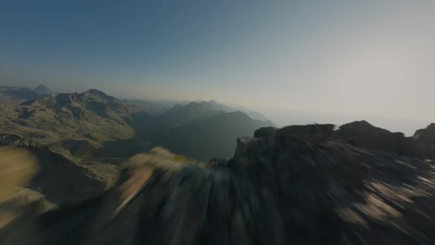 A breathtaking FPV drone speeds along a high-altitude rocky ridge, passing two hikers and soaring over the edge to reveal a stunning alpine valley