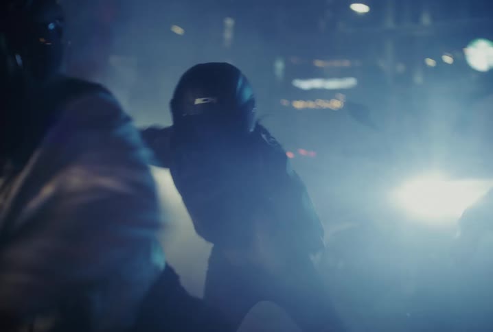 Faceless dancers in motorcycle helmets groove together in slow motion under the bright lights and smoke of a nightclub