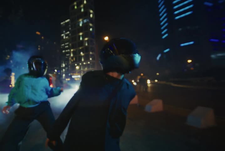 Dancers in motorcycle helmets perform a choreographed routine on a smoky city street at night in slow motion