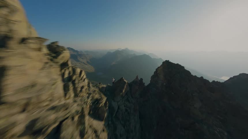Breathtaking FPV drone footage soars along a perilous mountain ridge, passing hikers and unveiling a majestic, expansive valley below