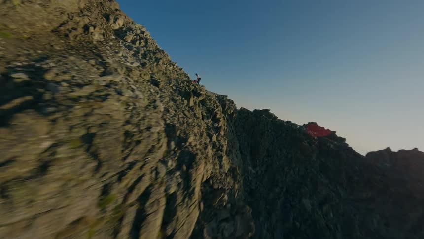 A thrilling FPV drone chase follows a hiker along a dramatic and exposed mountain ridge with stunning panoramic views