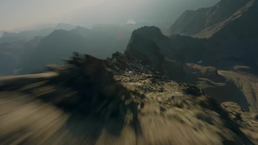 An adrenaline-fueled FPV drone flies low and fast over a rocky mountain peak into the misty sky