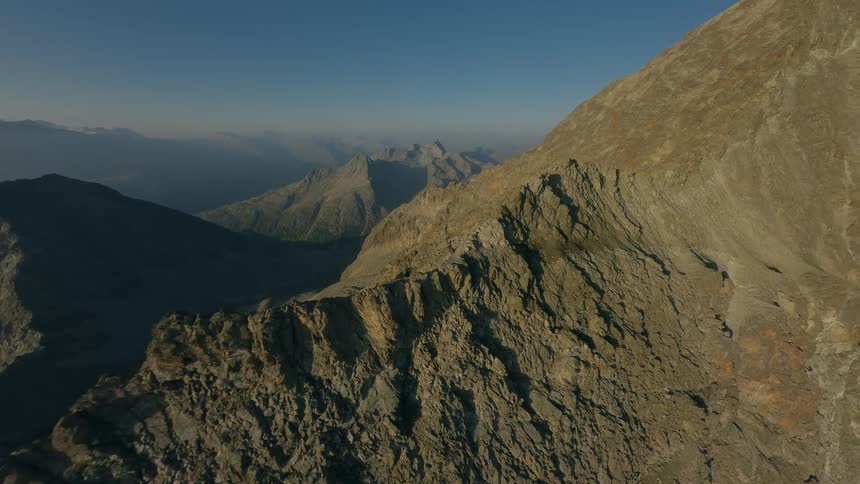 Aerial drone footage follows hikers trekking along a narrow, rocky mountain ridge during a beautiful sunrise