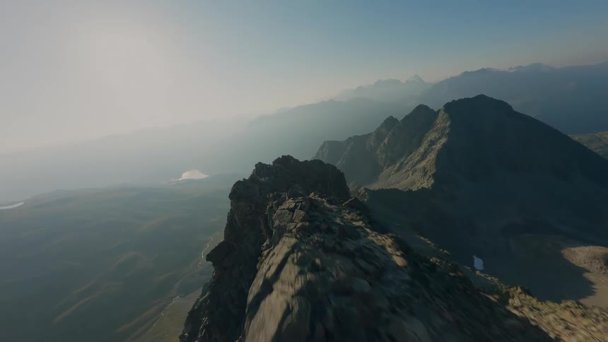 A thrilling FPV drone flight soars along a sharp, rocky mountain ridgeline against the hazy morning sun